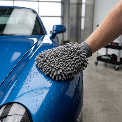 Person cleaning a blue car with a gray microfiber glove in a garage.