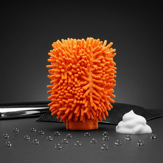 Orange microfiber glove cleaning pad with a small pile of white foam on a dark surface with water droplets.